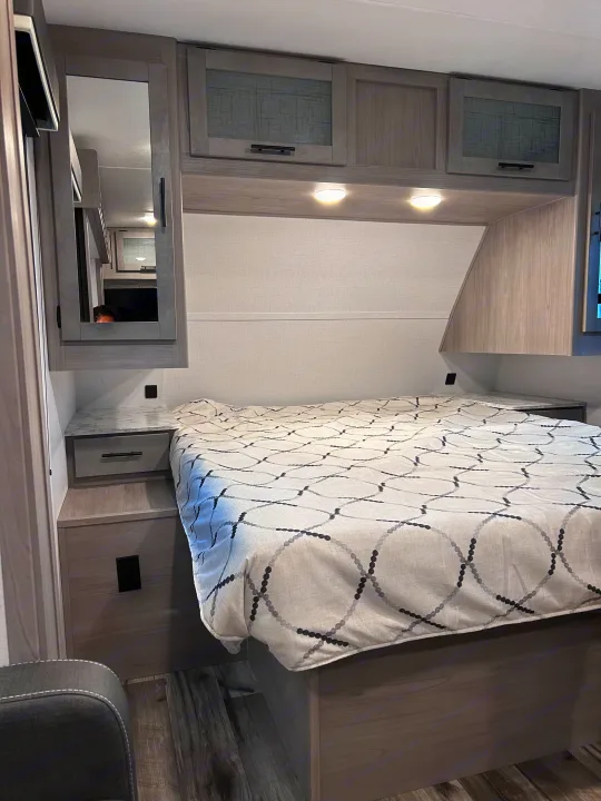 Modern RV rental bedroom featuring a comfortable bed, stylish overhead cabinets, and practical built-in nightstands.. 4YDTCMH25RJ935536 1805RB 2024