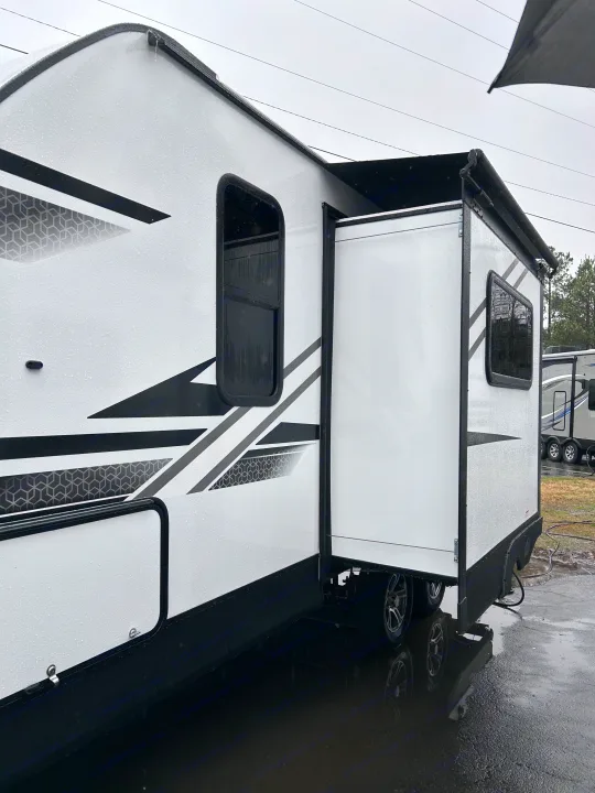 Detailed view of a white RV rental's exterior, featuring a deployed slide-out on a wet, overcast day.. 4YDTCMH25RJ935536 1805RB 2024