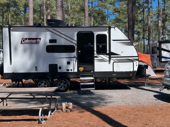 White Coleman rv rental travel trailer at a sunny campground site with picnic table & trees.. 4YDTCMH25RJ935536 1805RB 2024