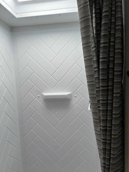 Clean, compact RV rental shower with white herringbone walls, a small shelf, and a dark patterned shower curtain.. 4YDTCMH25RJ935536 1805RB 2024