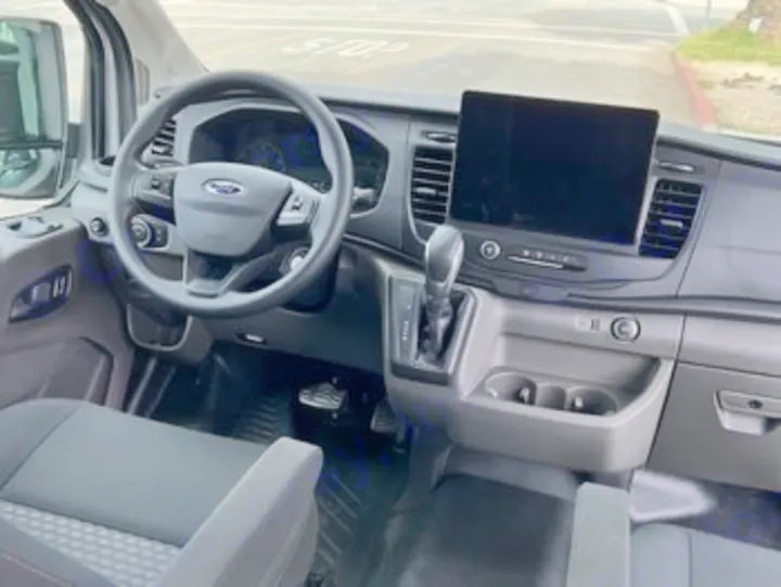 Inside an RV rental van: the functional driver's cockpit of a Ford Transit. Features a modern steering wheel & large vertical screen.. Ford Transit 2023