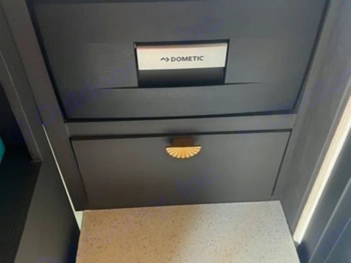 Dark gray Dometic RV refrigerator drawer and a lower storage cabinet with gold handle, in an RV rental.. Ford Transit 2023