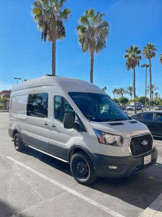 RV rental: Light grey Ford Transit camper van in a sunny parking lot with palm trees.. Ford Transit 2023