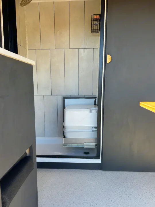 RV rental bathroom with modern grey tiles, shower, and space-saving pull-out portable toilet on sliders.. Ford Transit 2023