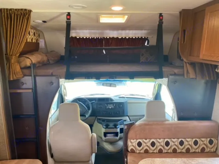 Inside an RV rental, this view shows the cab-over bed above the cockpit and front seats, revealing a compact sleeping and driving area.. Coachmen Leprechaun 2017