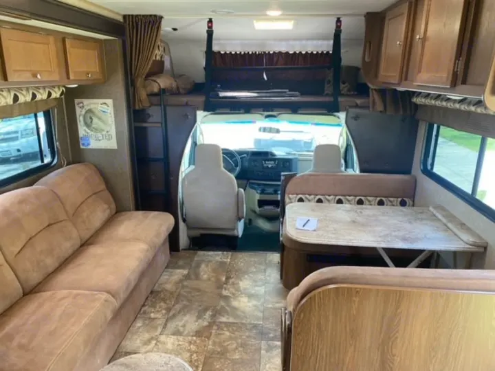 Spacious RV rental interior with a comfortable living area (couch), dining table, and overhead bunk, ready for your adventures.. Coachmen Leprechaun 2017