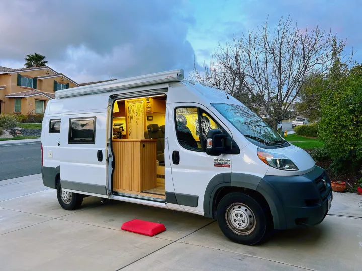 White Ram ProMaster **rv rental** van conversion with lit interior and extended awning, parked on a driveway.. Ram promaster 2500 2017