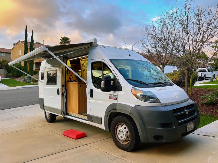 Experience van life! This white Ram ProMaster camper van, an ideal rv rental, shows its open, cozy interior and extended awning.. Ram promaster 2500 2017