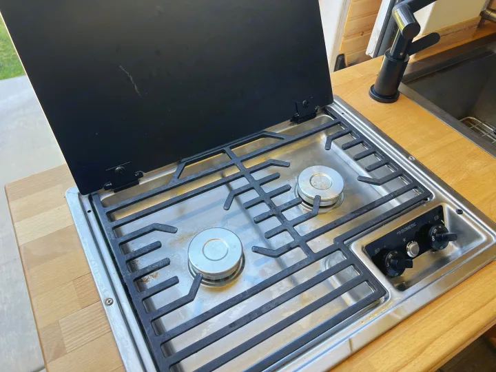 Compact Dometic stove & sink in an RV rental kitchen. Features a two-burner cooktop, black cover, and wood counter.. Ram promaster 2500 2017