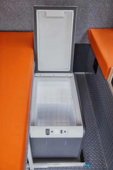 RV rental convenience: Top-loading portable fridge/freezer, open, empty, between orange benches and textured walls in a camper van interior.. Gmc sierra 1500 2024