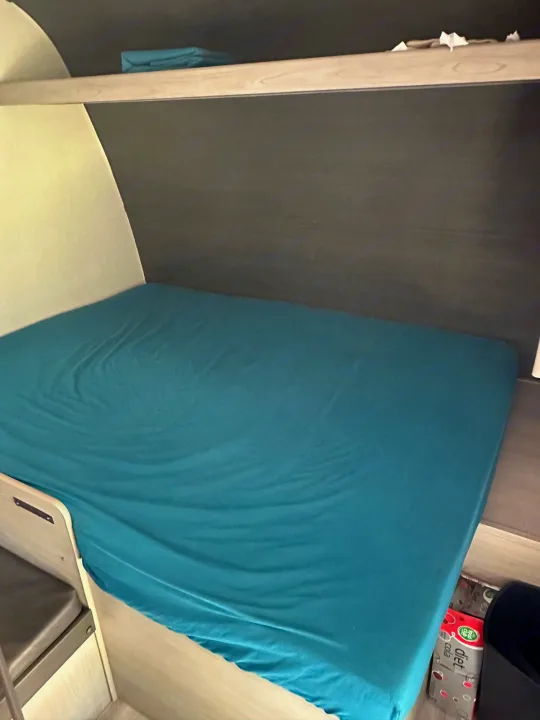 Cozy RV rental interior: A bed with a teal sheet, overhead shelf, and visible storage for a comfortable sleeping area.. Keystone RV Springdale 2024