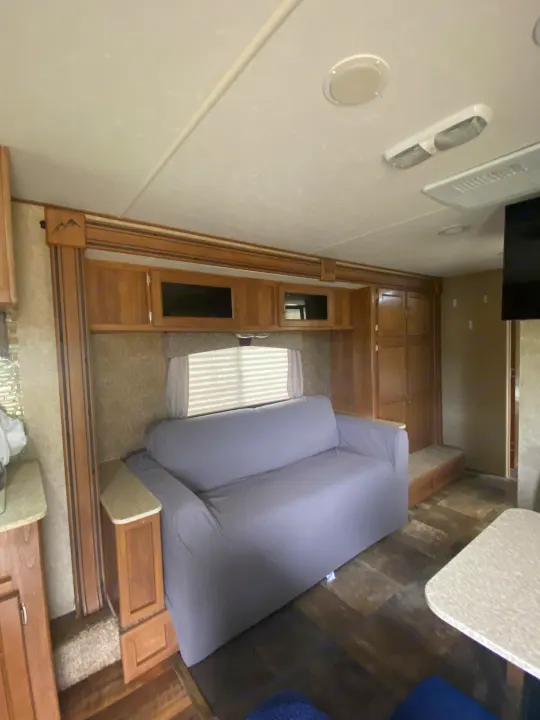 Spacious RV rental interior with a gray sofa, wood cabinets, and plank flooring. Ideal for comfortable travel.. Coachmen Apex 2014