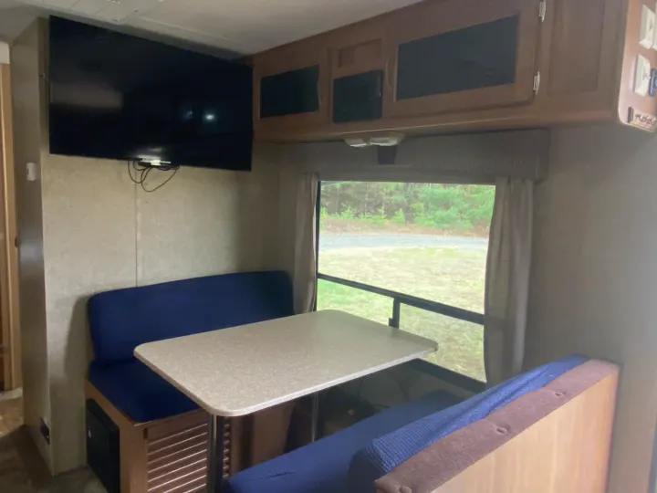 Cozy RV rental interior featuring a dinette with blue seats, a wall-mounted TV, and overhead cabinets.. Coachmen Apex 2014