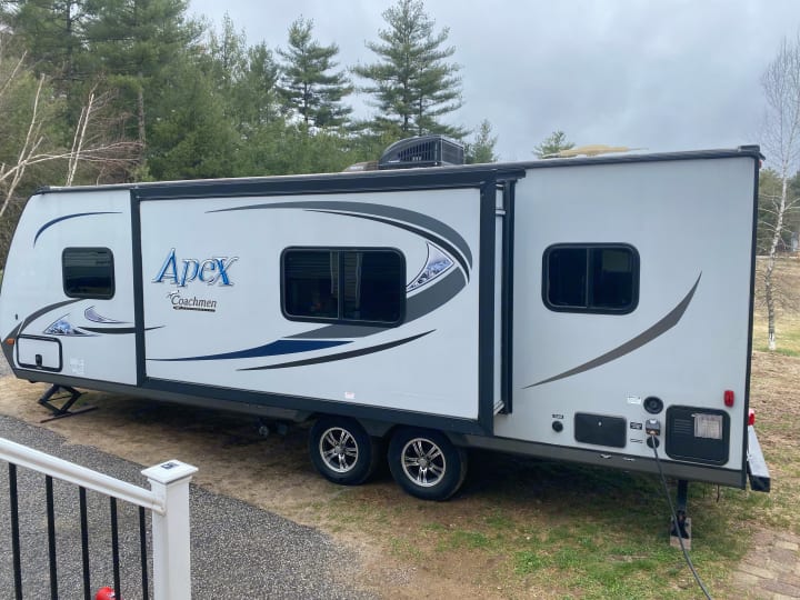 A clean, white Apex Coachmen rv rental parked on gravel with its slide-out extended, ready for adventure amidst the trees.. Coachmen Apex 2014