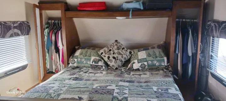 Inside an RV rental, a cozy bedroom features a nature-themed quilt, ample storage wardrobes, and window blinds.. Forest River Salem Cruise Lite 2018