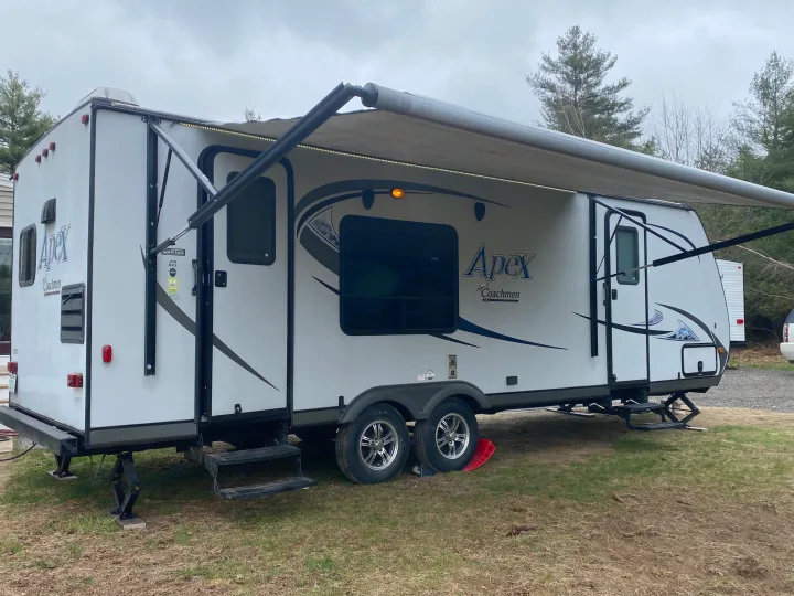 White Apex Coachmen RV rental with extended awning and leveling jacks, parked on grass for an outdoor adventure.. Coachmen Apex 2014