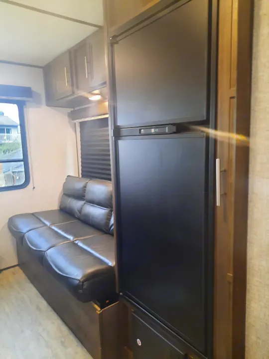 RV rental interior: A practical living space with a black leather sofa, large black refrigerator, and overhead cabinets.. Dutchmen Aspen 2020