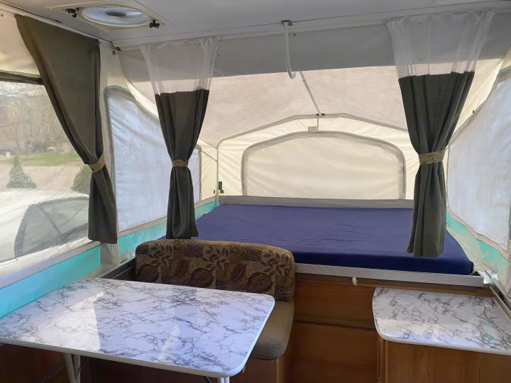 Inside this pop-up RV rental: a comfy bed, dining area with a marble table, and soft curtains.. Palomino Real - Lite 801 2007