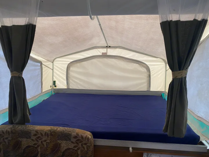 Inside this **RV rental** pop-up camper, a neat bed with blue sheets and tied dark curtains offers a cozy retreat. An "EXIT" sign is visible.. Palomino Real - Lite 801 2007