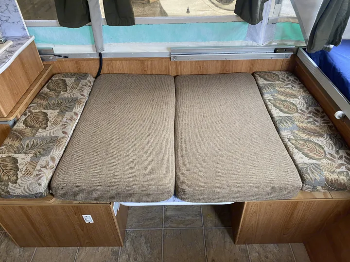 RV rental interior: A cozy dinette with patterned & neutral cushions, convertible to a bed, set against wood paneling.. Palomino Real - Lite 801 2007