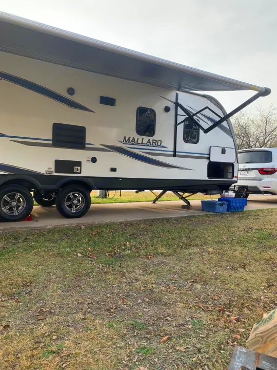 A white 'Mallard' travel trailer, likely an RV rental, is parked at a campsite with its awning extended, ready for outdoor adventures.. Heartland RVs Mallard 2021