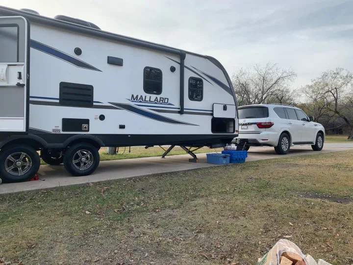 White Mallard RV rental and SUV parked at a serene campground, ready for outdoor travel.. Heartland RVs Mallard 2021