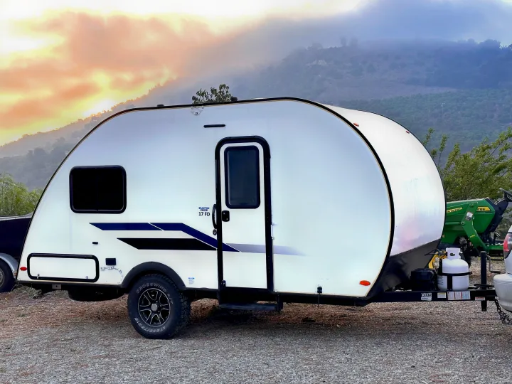 White Braxton Creek 17 FD travel trailer (RV rental) parked on gravel, with a vibrant sunset and misty mountains.. Braxton Creek Bushwhacker Plus 2022