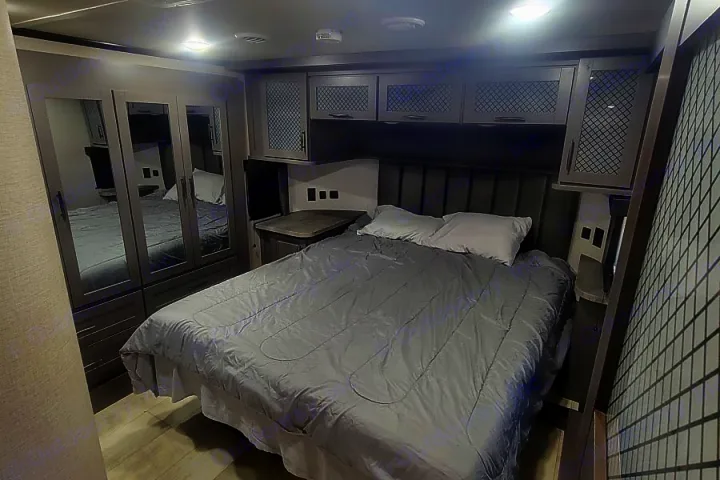 Modern RV rental bedroom with a large bed, stylish grey cabinets, mirrored wardrobes, and contemporary decor for your travels.. Grand Design Momentum M-Class Toy Hauler 2022