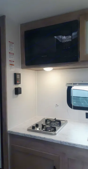 An RV rental's well-equipped kitchenette: sleek Greystone microwave, compact gas stove, and marbled counter.. Grand River 22MB 2024