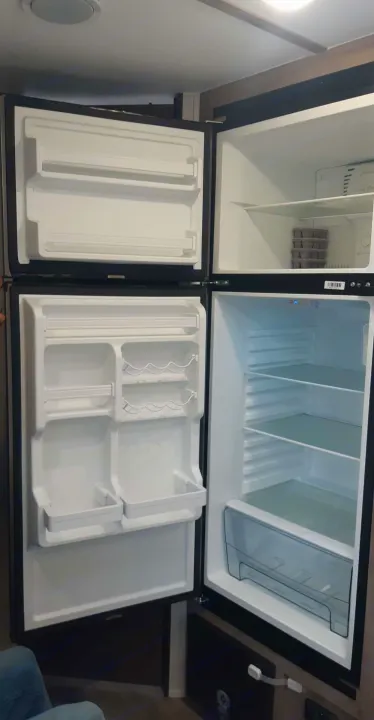 Spacious, clean RV rental refrigerator and freezer, open to reveal empty shelves and door storage, ready for use.. Grand River 22MB 2024