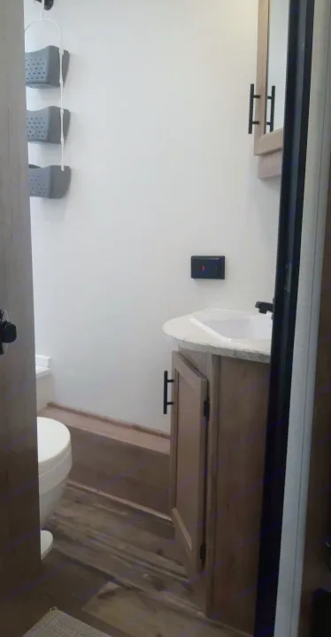 Compact RV rental bathroom: features toilet, sink vanity, and wall-mounted storage baskets for efficiency.. Grand River 22MB 2024