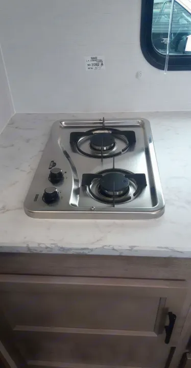 View inside an RV rental showing a compact two-burner gas cooktop on a marble-patterned countertop.. Grand River 22MB 2024