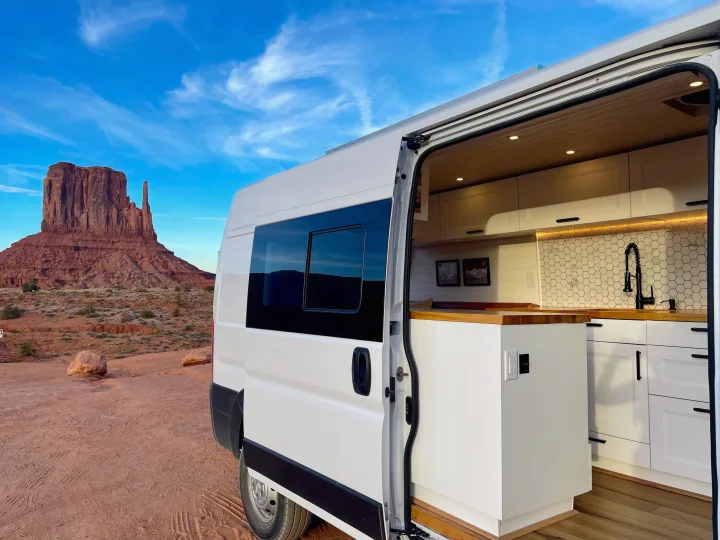 White RV rental with open side door showcasing its modern kitchen, parked in the red desert of Monument Valley.. Dodge Ram ProMaster 2500 2021