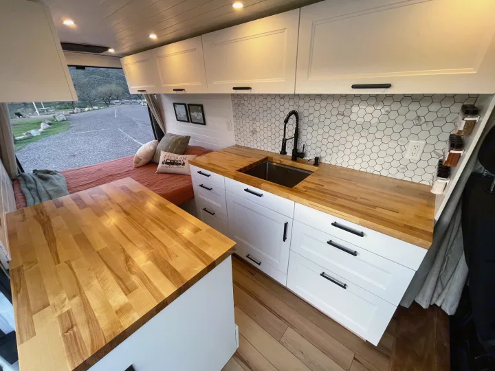 Spacious RV rental interior featuring a modern kitchen with wood counters, white cabinets, hex backsplash, and a cozy bed area.. Dodge Ram ProMaster 2500 2021