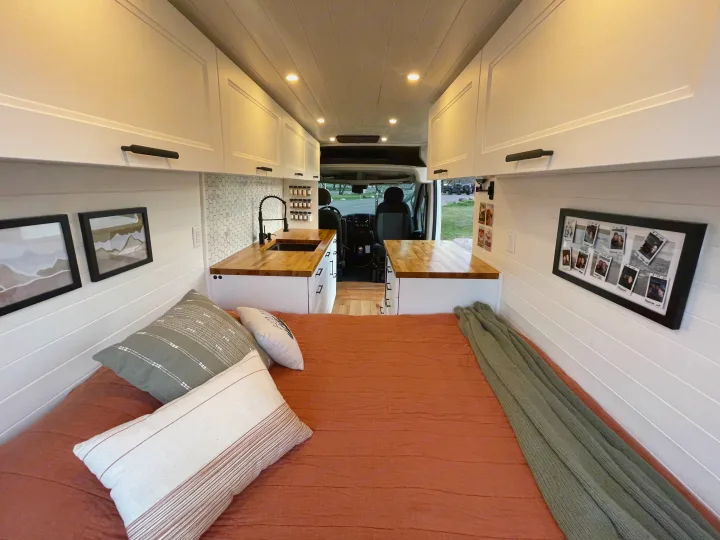 Cozy RV rental interior featuring a bed, kitchen, overhead cabinets, and stylish decor for mobile living.. Dodge Ram ProMaster 2500 2021