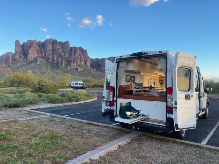 Experience van life! This RV rental features an open campervan with an outdoor kitchen, parked against stunning desert mountains.. Dodge Ram ProMaster 2500 2021