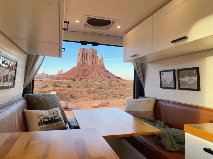 Cozy RV rental interior with brown leather seating, wooden tables, and a stunning open-door view of Monument Valley.. Dodge Ram ProMaster 2500 2021