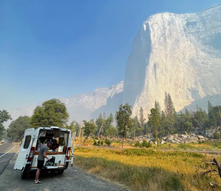 Yosemite RV rental: A traveler prepares food in a van's open kitchen, with majestic El Capitan towering above.. Dodge Ram ProMaster 2500 2021