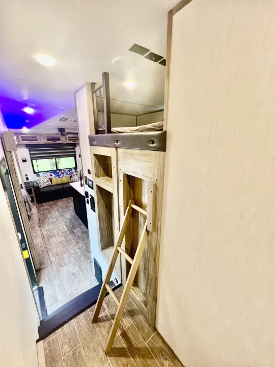 Experience this RV rental's versatile interior: a bunk bed with ladder overlooks a modern living area, sofa, and bright lighting.. Forest River Cherokee Arctic Wolf 2021
