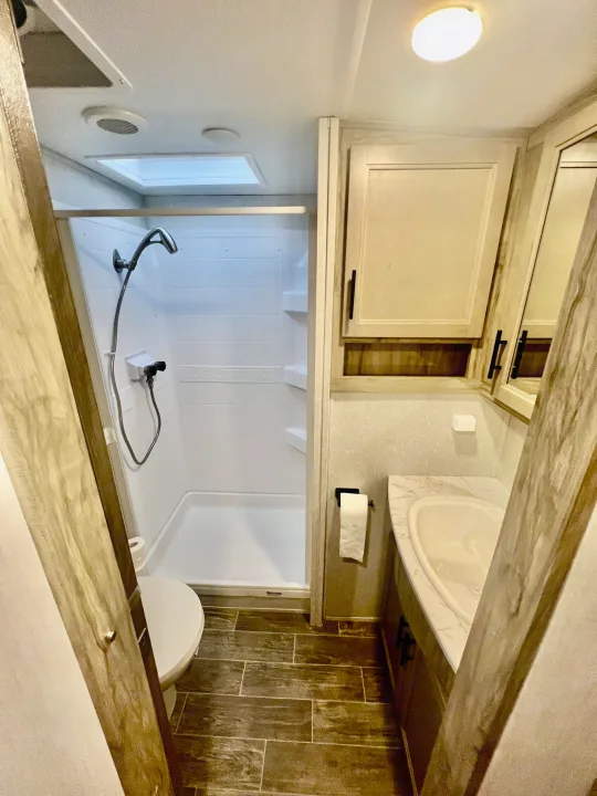 RV rental bathroom interior with a bright shower, toilet, and corner vanity with sink and mirror.. Forest River Cherokee Arctic Wolf 2021