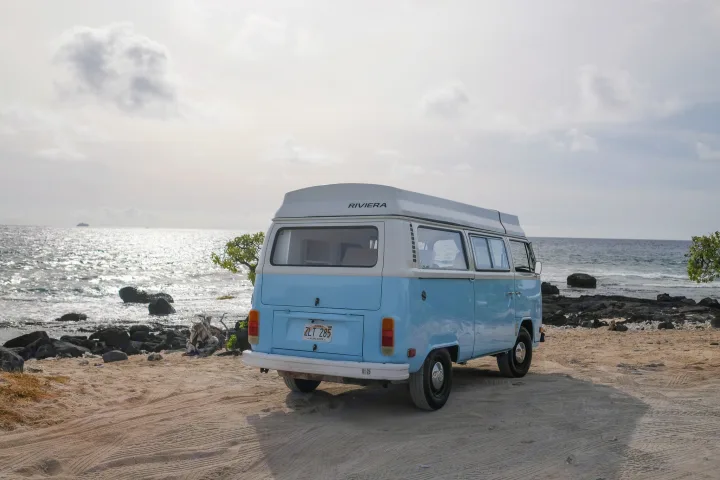 Experience island life! This classic blue and white VW camper van, perfect as an RV rental, rests on a Hawaiian beach by the ocean.. Volkswagen T2 Westfalia 1976