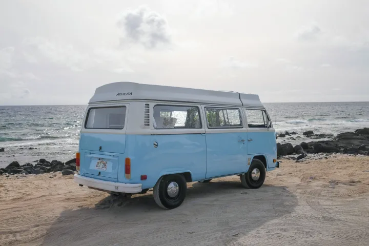 Blue and white VW camper van, ideal RV rental, parked on a sandy Hawaiian beach by the ocean.. Volkswagen T2 Westfalia 1976