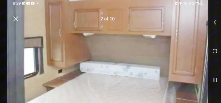 View inside an RV rental bedroom showing a bed with a protective mattress cover, wood overhead cabinets, and a side window.. StarCraft autumn ridge 2014