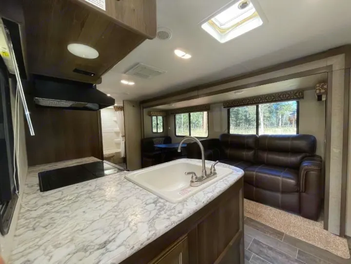 RV rental interior: kitchen with sink & stovetop, comfortable living area with brown sofa and large windows. Bright, spacious camper.. Keystone Bullet Ultra 2018
