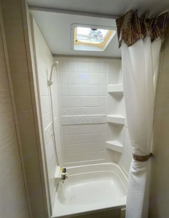 Compact RV rental bathroom features a small tub, handheld shower, and ceiling vent.. Keystone Bullet Ultra 2018