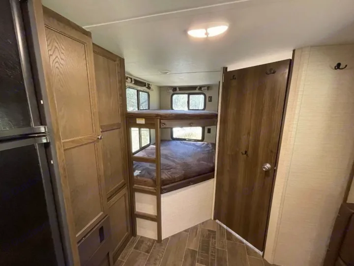 This RV rental interior features cozy bunk beds on the right, with a fridge and cabinets on the left, ideal for family trips.. Keystone Bullet Ultra 2018