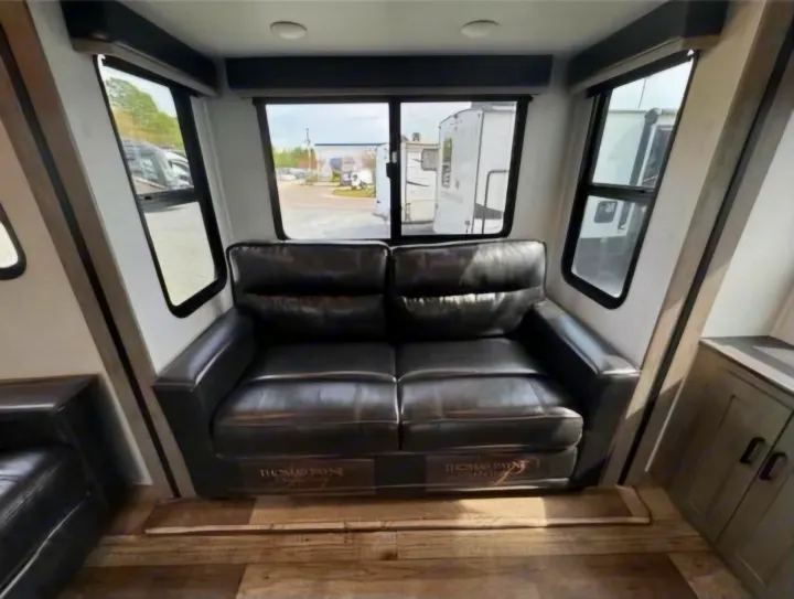 Cozy RV rental living space featuring a black leather sofa and large windows looking out to other vehicles.. Keystone RV Outback 2021