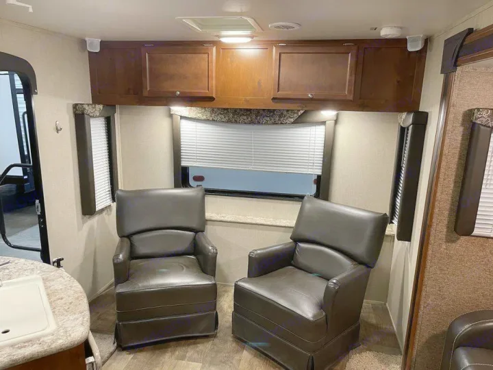 This **rv rental** shows a cozy interior with two brown recliners, overhead wooden cabinets, and windows with blinds.. gulfstream Streamlite 2016