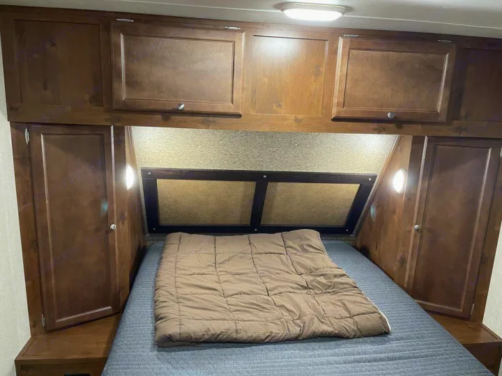 Cozy RV rental bedroom with ample wooden storage cabinets, a comfortable bed, and convenient lighting.. gulfstream Streamlite 2016
