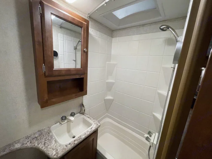 Inside an RV rental: a compact bathroom with a sink, mirrored cabinet, and white-tiled shower.. gulfstream Streamlite 2016